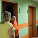 Senior woman engages in conversation with caregivers in a facility corridor.